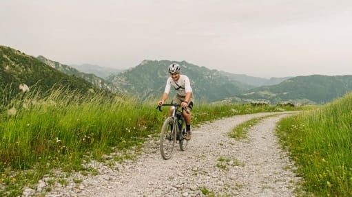 Ciclista atravesando un camino de grava entre montañas y prados