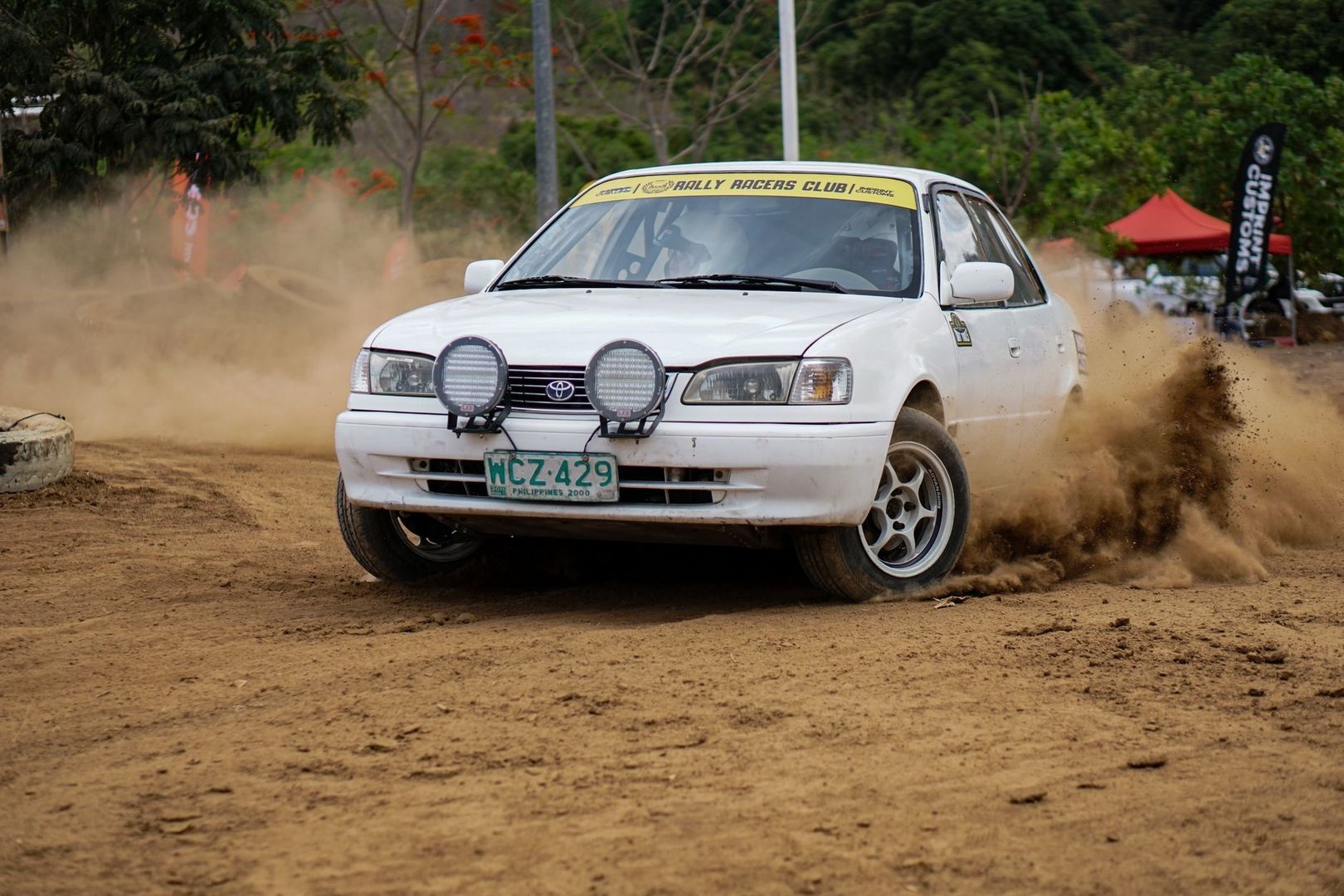 Coche de rally blanco derrapando y levantando polvo en una curva